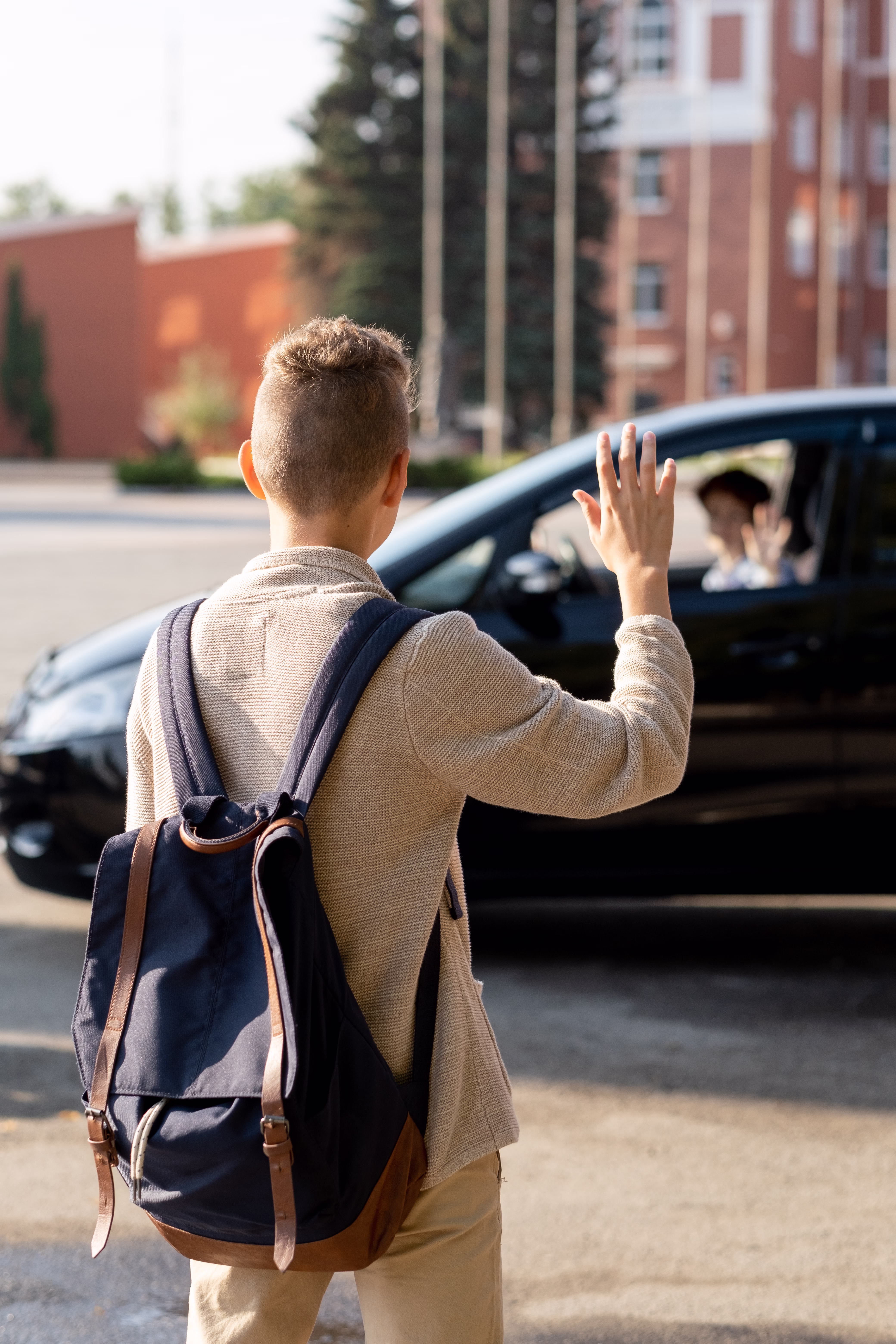 Back view of schoolboy with backpack waving hand to his parent no car FR44